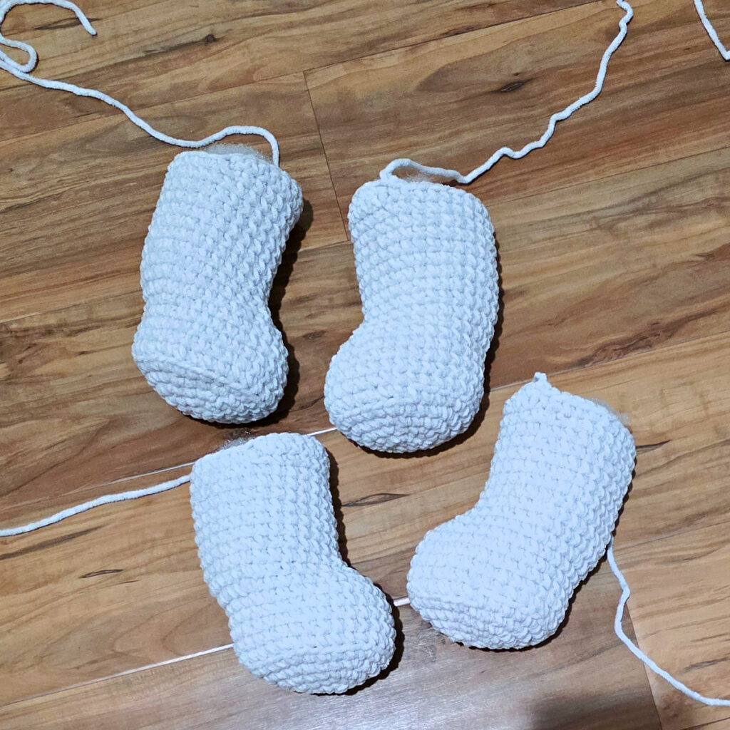 Four gray crochet amigurumi legs on a wooden floor.