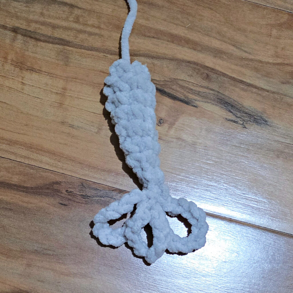 A gray tail for an elephant plushie in progress on a wooden floor.
