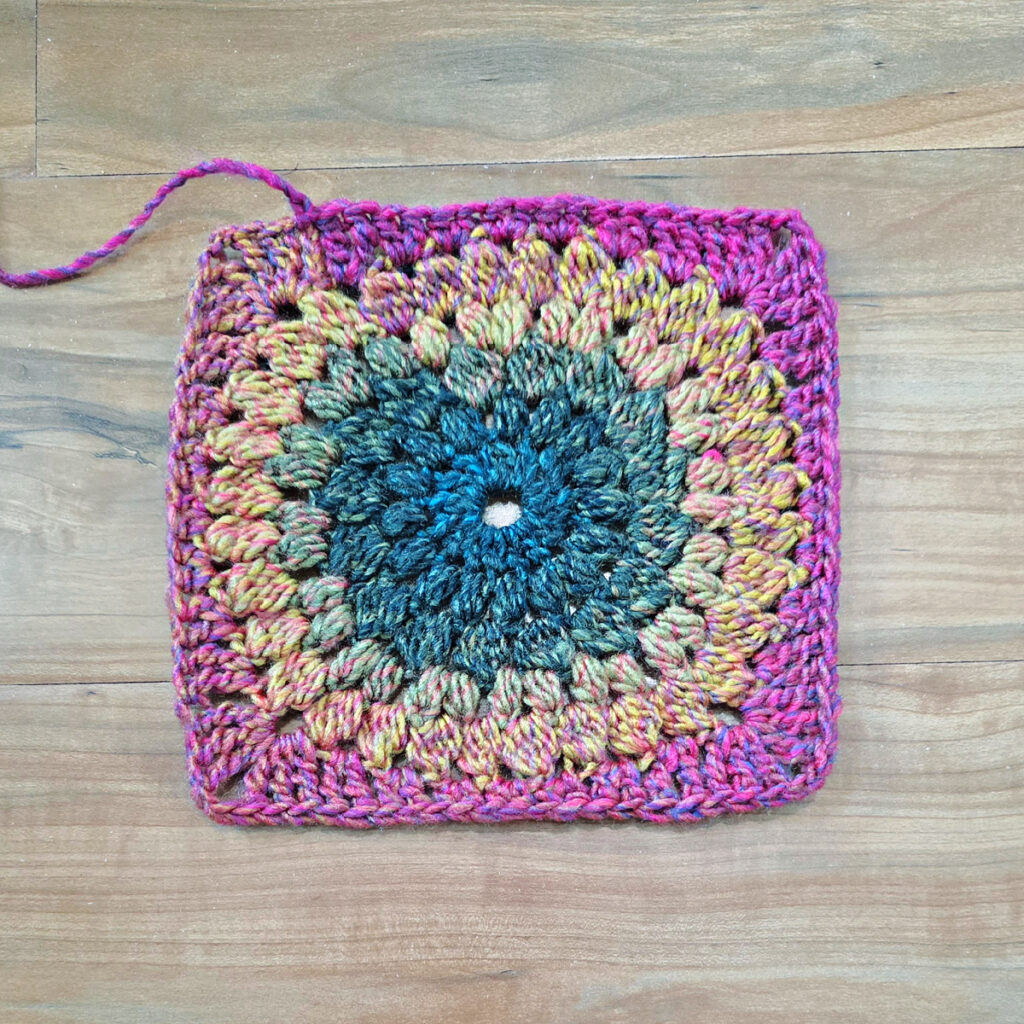 Colorful crochet floral square on a wooden background.