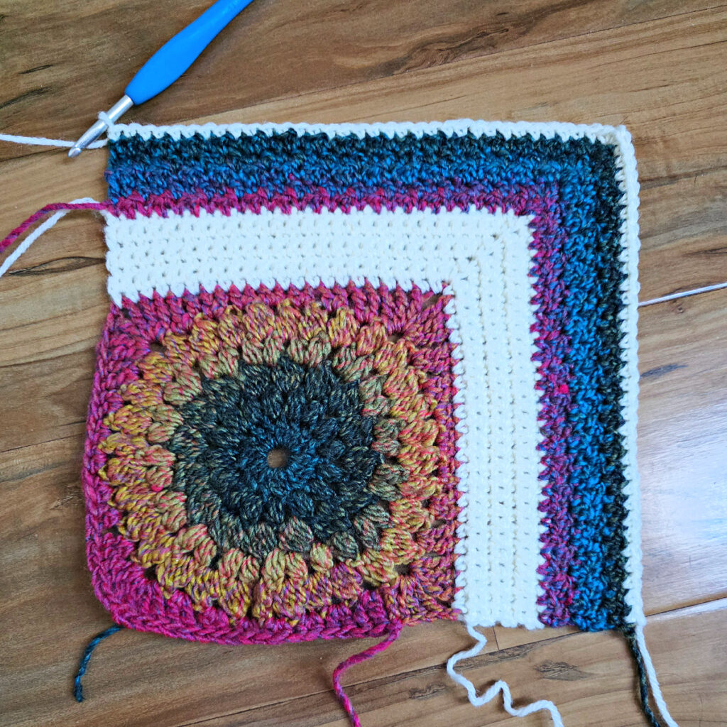 Finishing the last section of a colorful crochet blanket square.