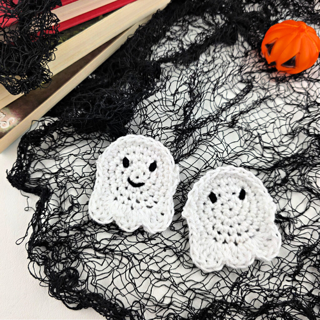Two crochet ghosts on a black net with a stack of books in the corner.