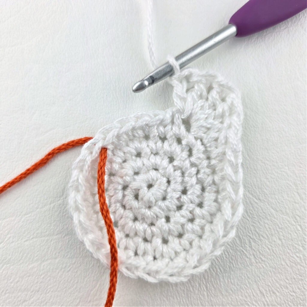 A white crochet circle with a purple hook and green yarn to mark the stitch.
