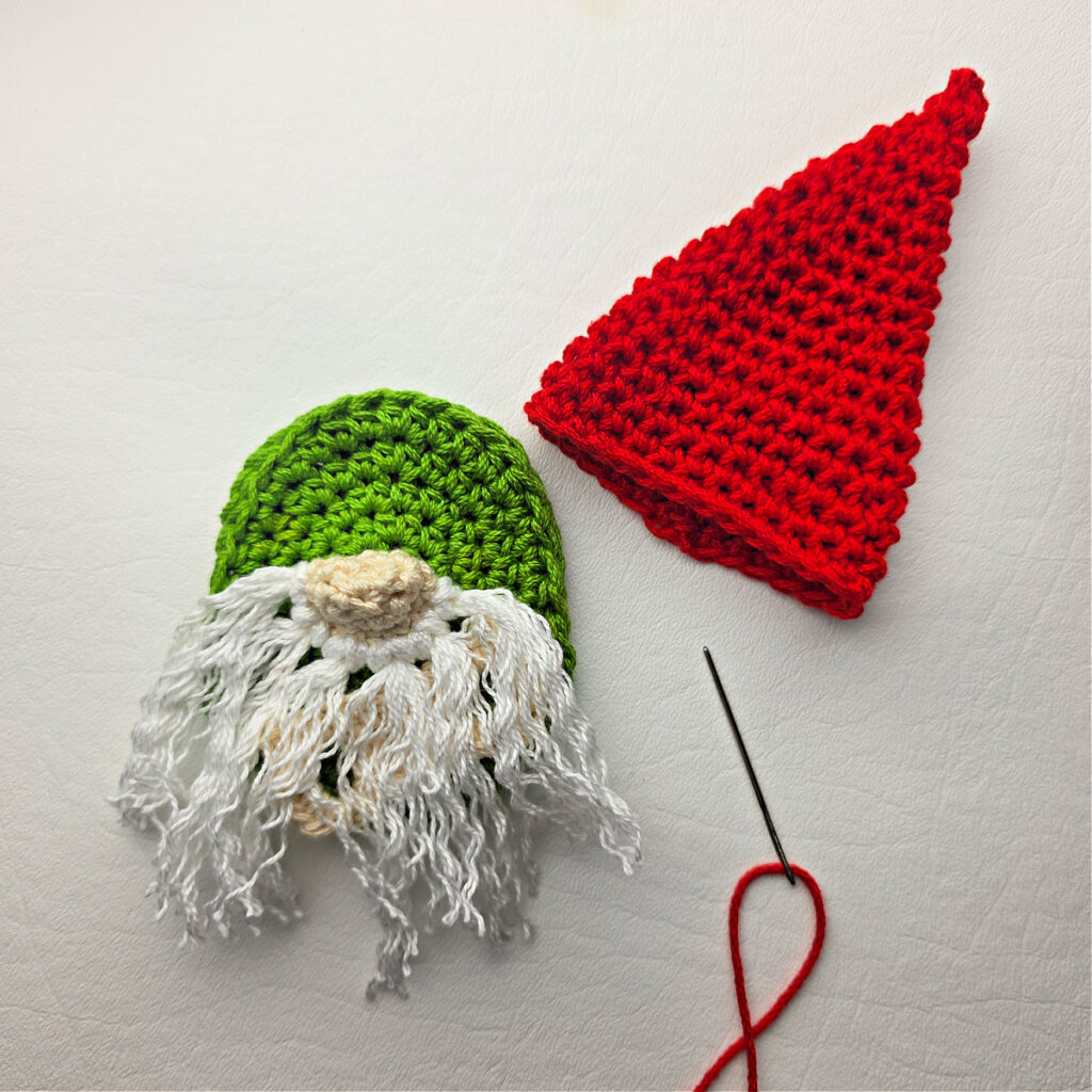 Seaming a Santa hat on a crochet gnome with a white beard.