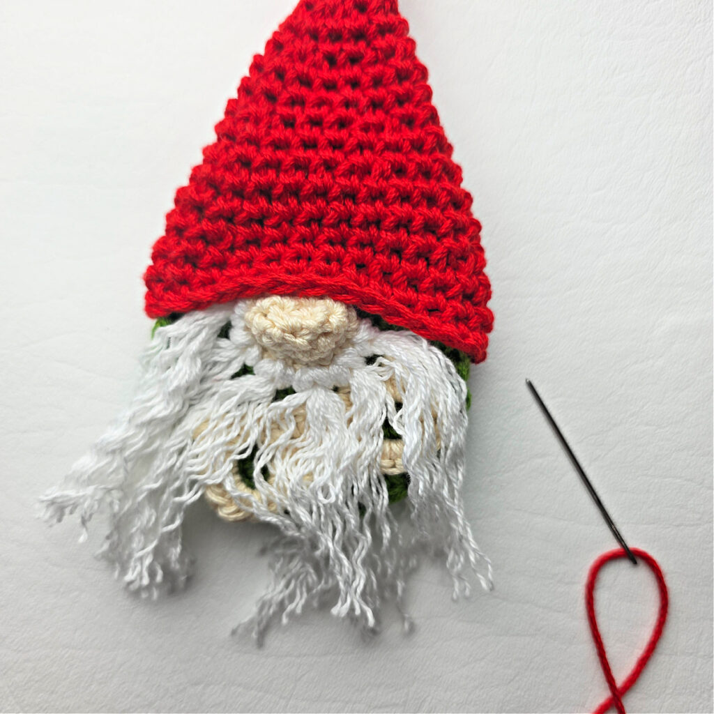 Seaming a Santa hat on a crochet gnome with a white beard.