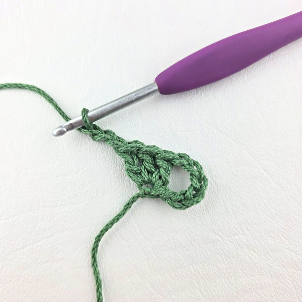 Round 1 of crochet granny stitch triangle with a purple crochet hook.