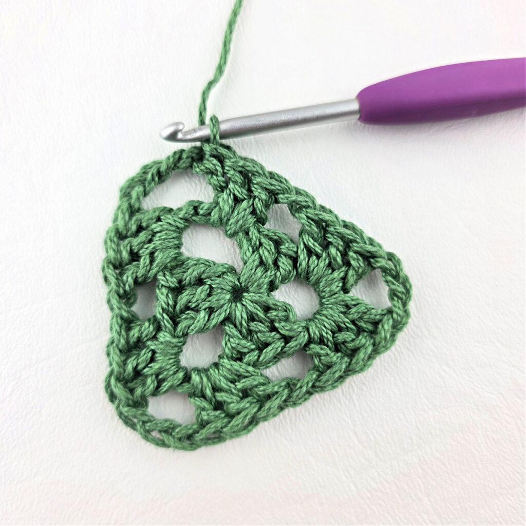 Round 2 of crochet granny stitch triangle with a purple crochet hook.