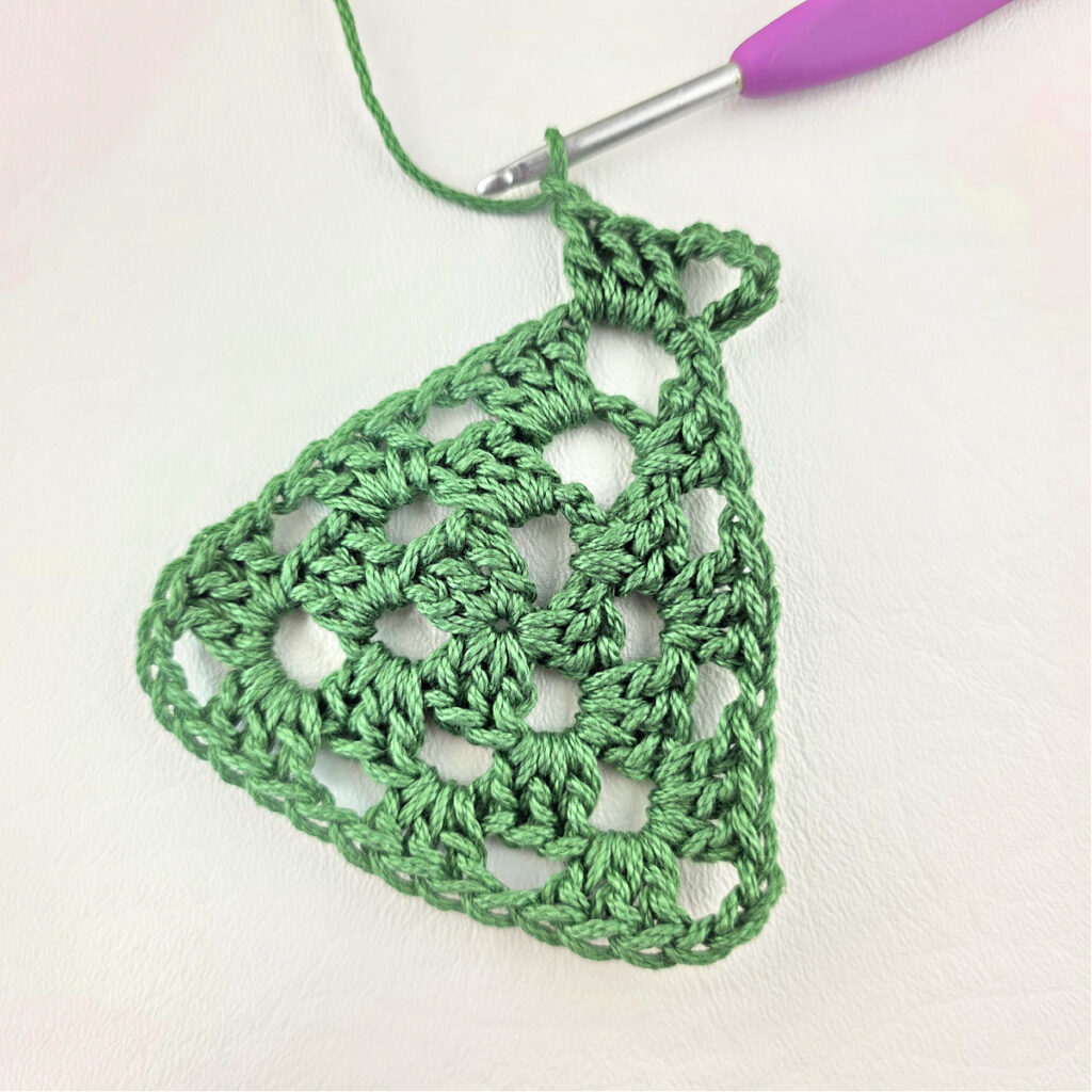Round 4 of crochet granny stitch triangle with a purple crochet hook.