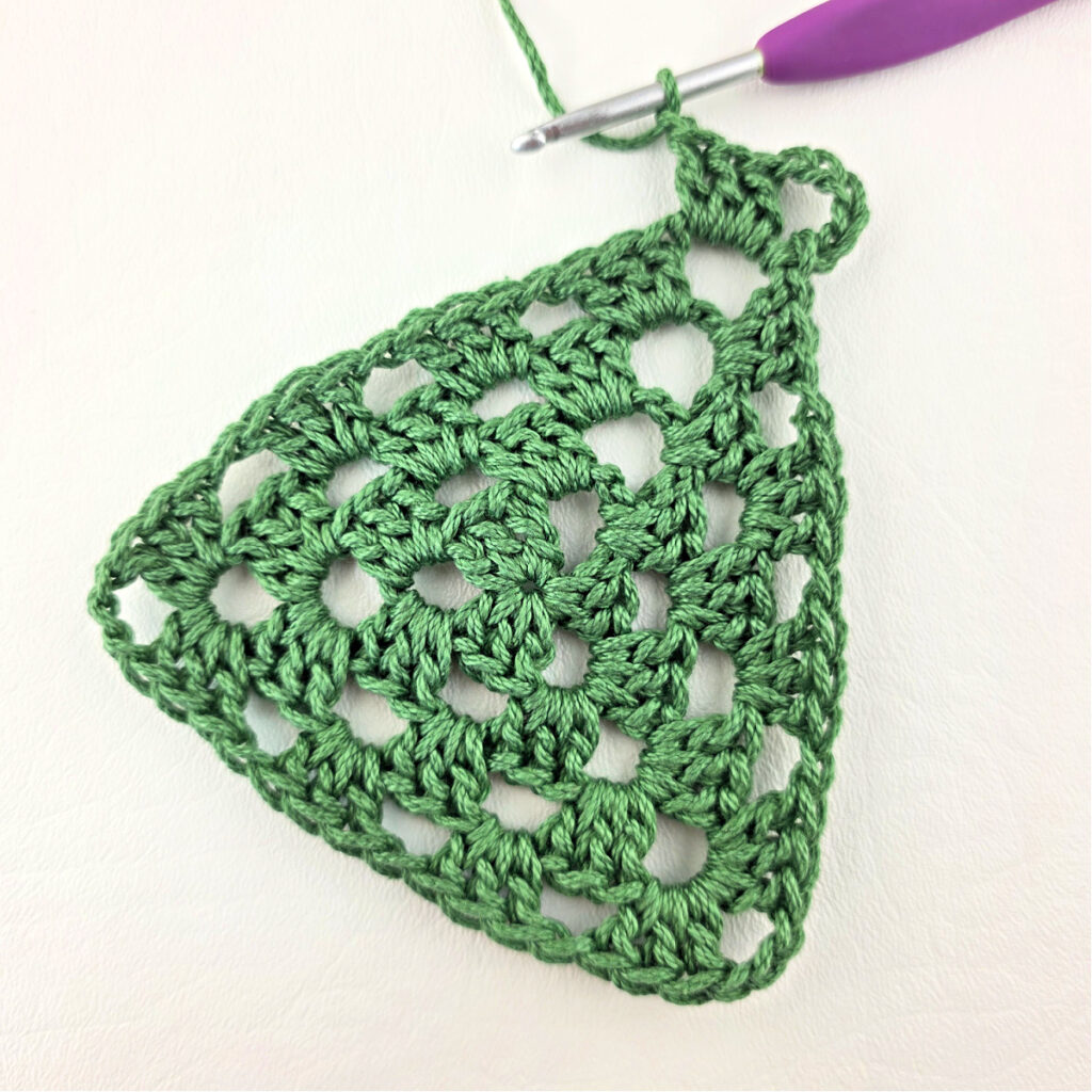 Round 4 of crochet granny stitch triangle with a purple crochet hook.