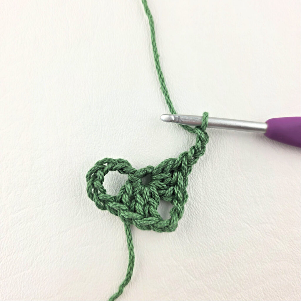 Round 1 of crochet granny stitch triangle with a purple crochet hook.