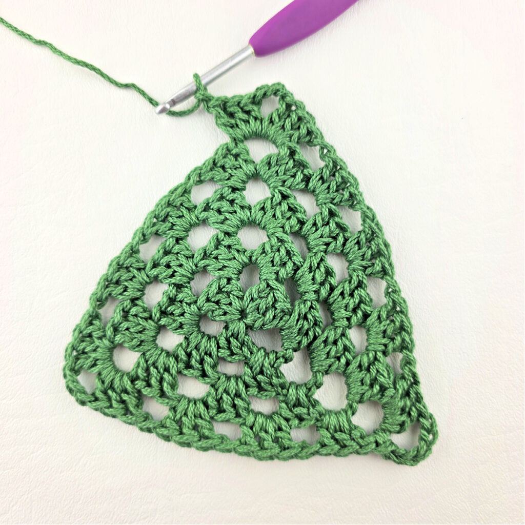 Round 5 of crochet granny stitch triangle with a purple crochet hook.
