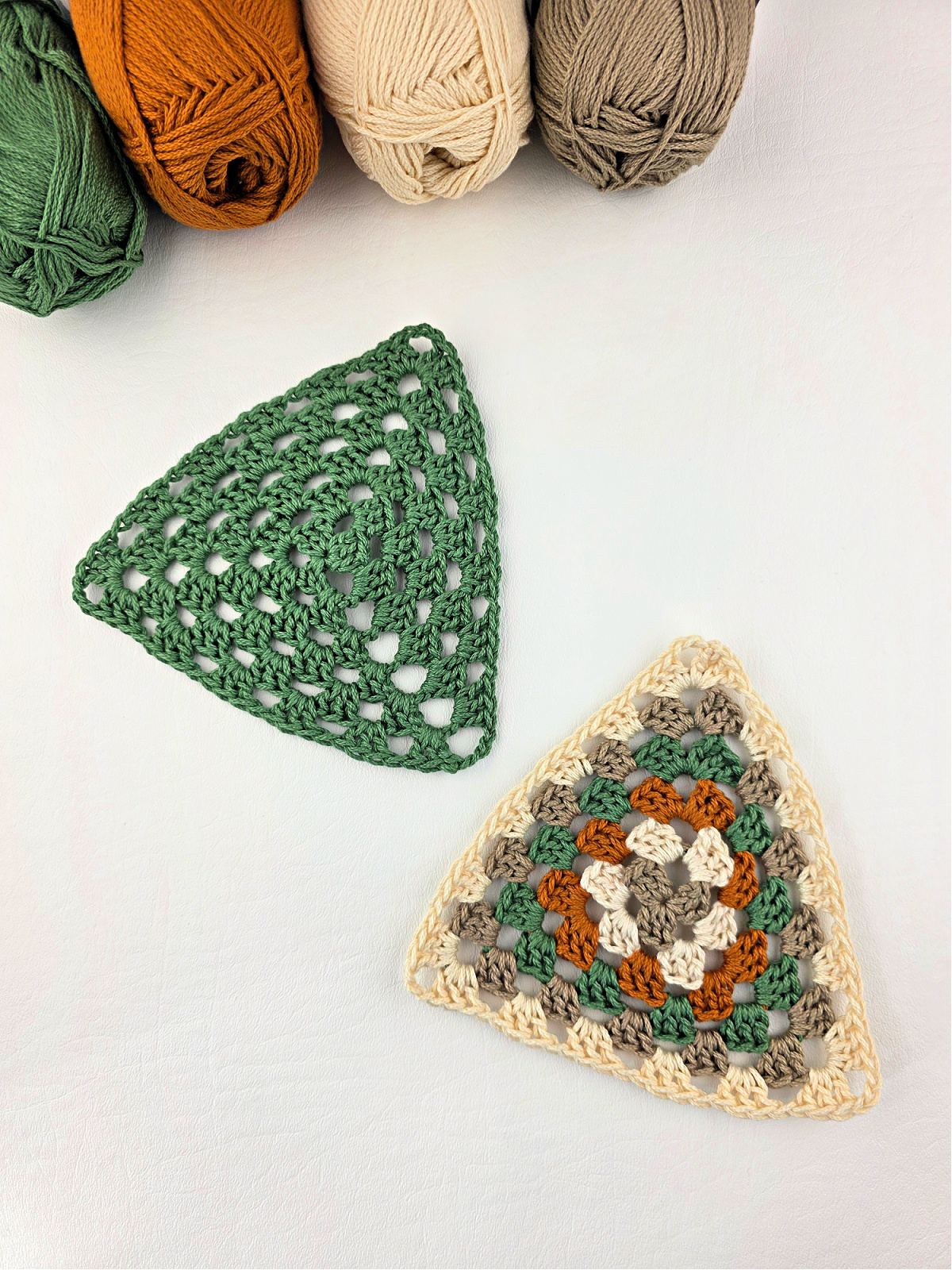 Solid green and multicolored crochet granny triangles on a white background with balls of yarn in the corner.
