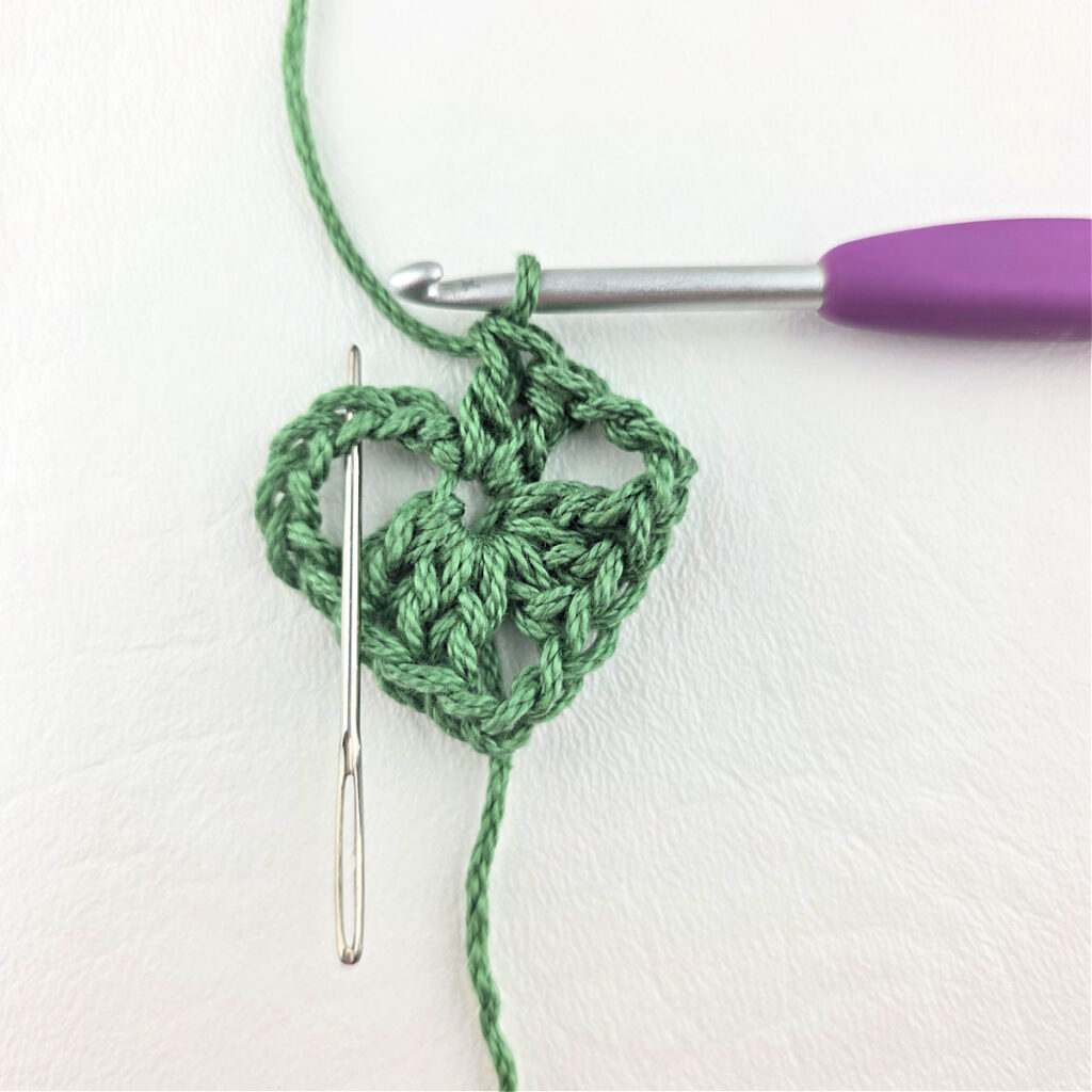 Round 1 of crochet granny stitch triangle with a purple crochet hook.
