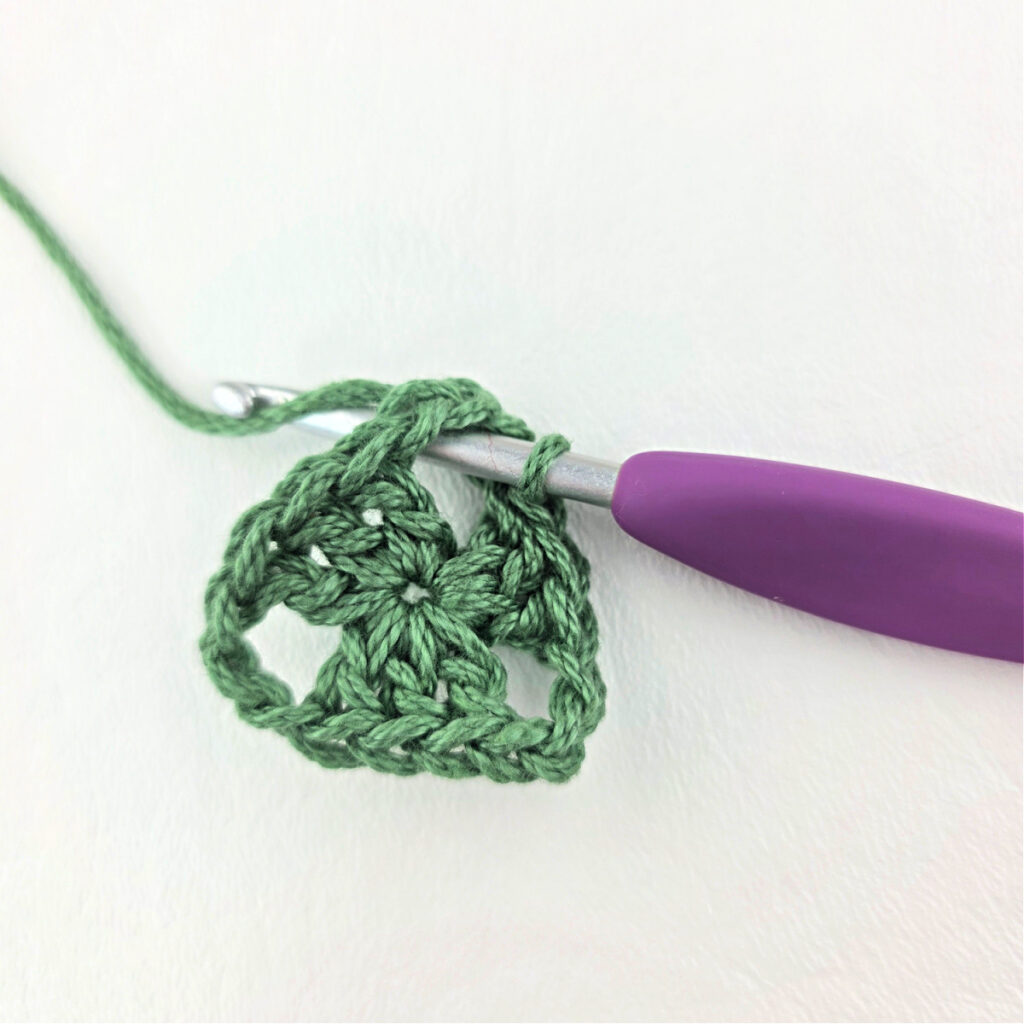 Round 1 of crochet granny stitch triangle with a purple crochet hook.