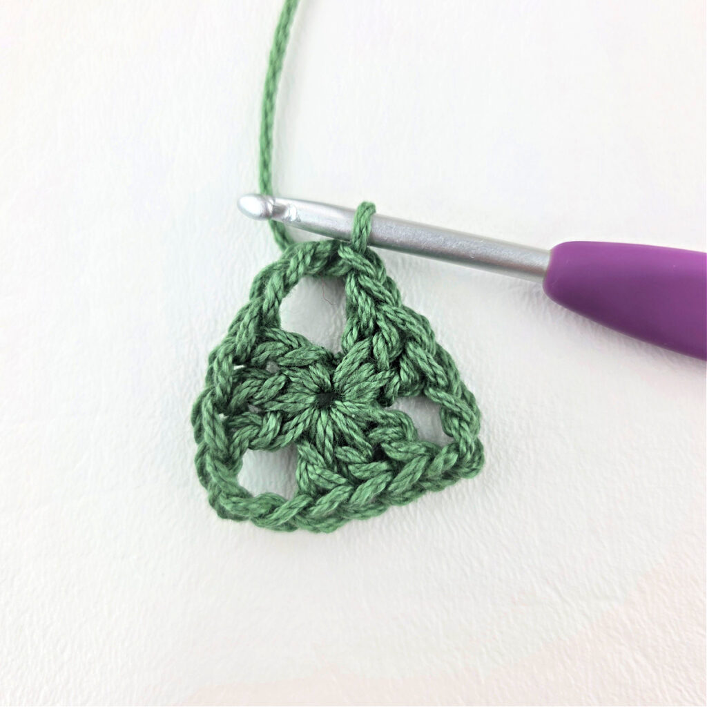 Round 1 of crochet granny stitch triangle with a purple crochet hook.
