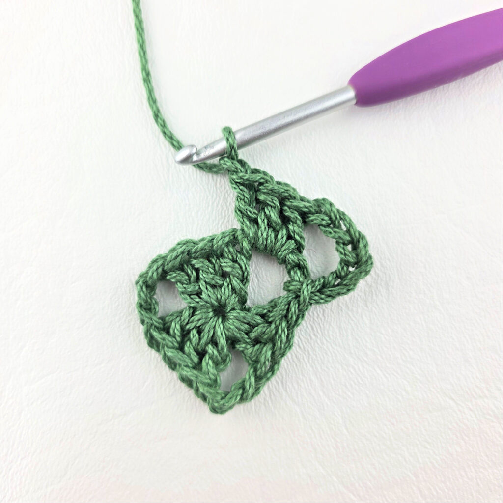 Round 2 of crochet granny stitch triangle with a purple crochet hook.