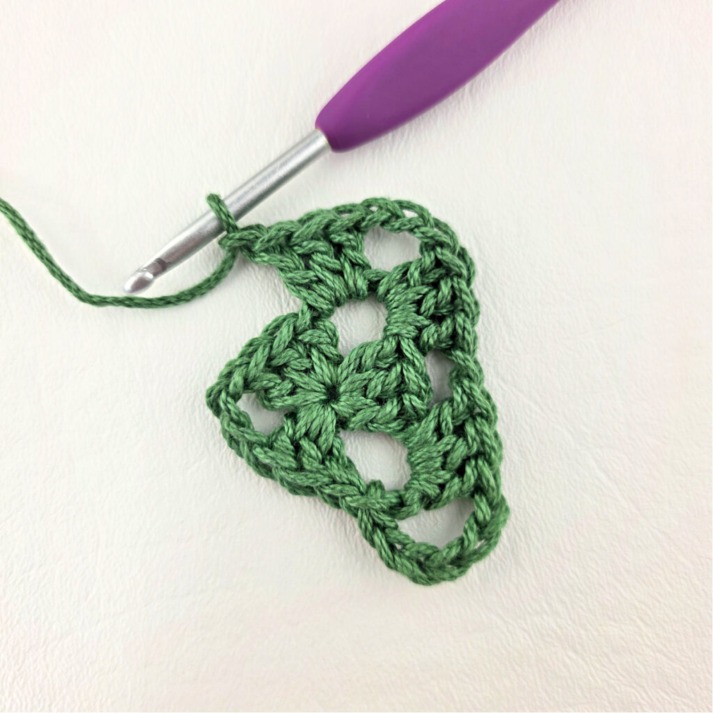 Round 2 of crochet granny stitch triangle with a purple crochet hook.