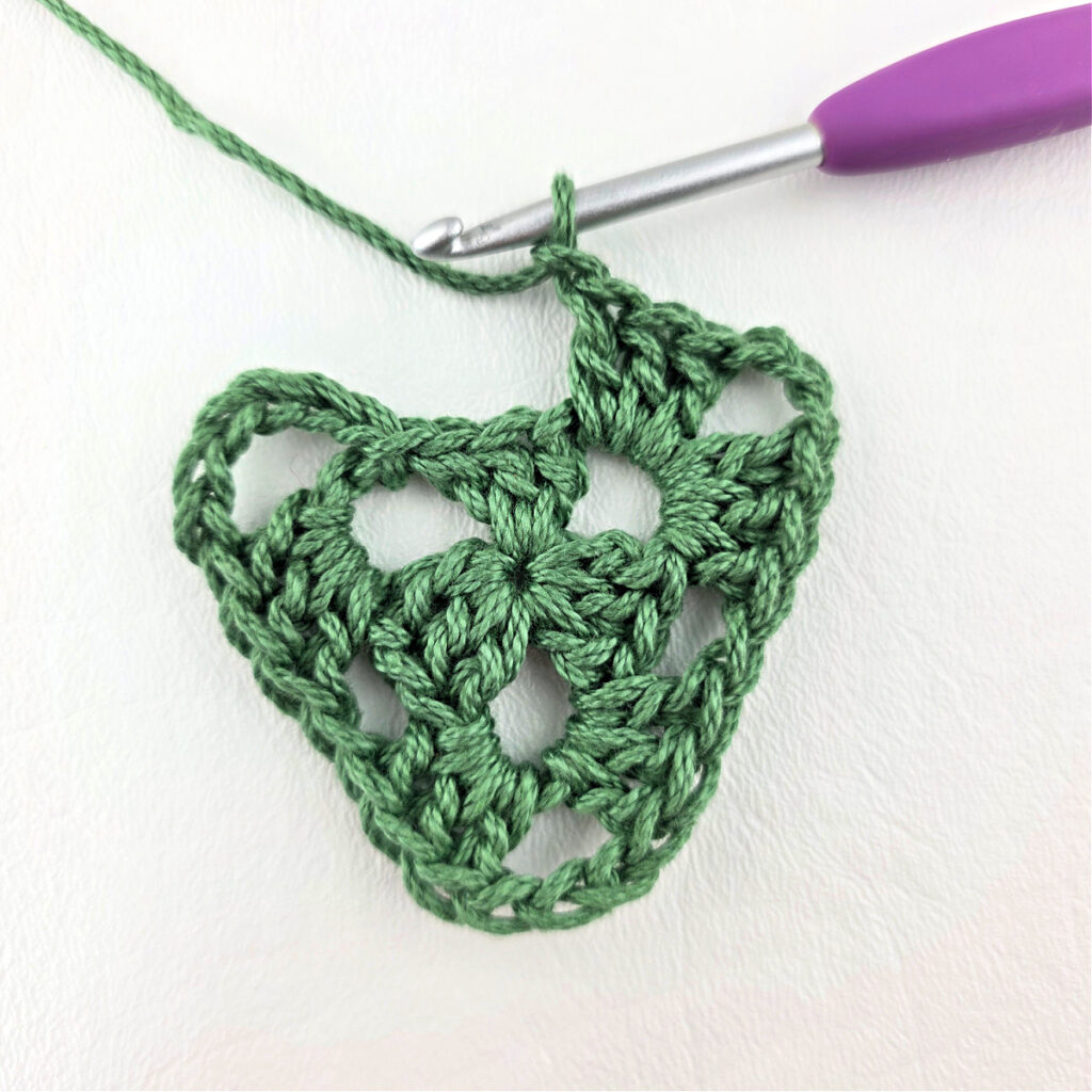 Round 2 of crochet granny stitch triangle with a purple crochet hook.