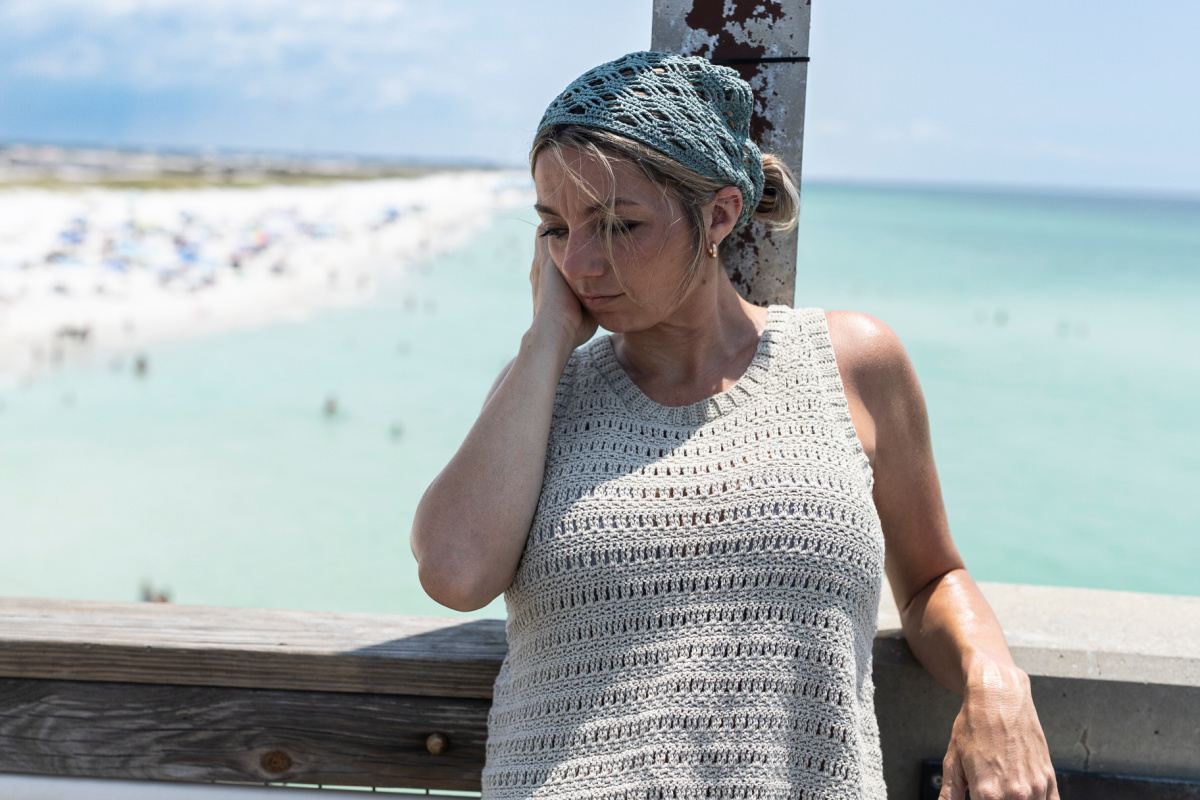 Girl leaning against a bridge wearing a grey crochet top with her hair tied back under a blue crochet head scarf.