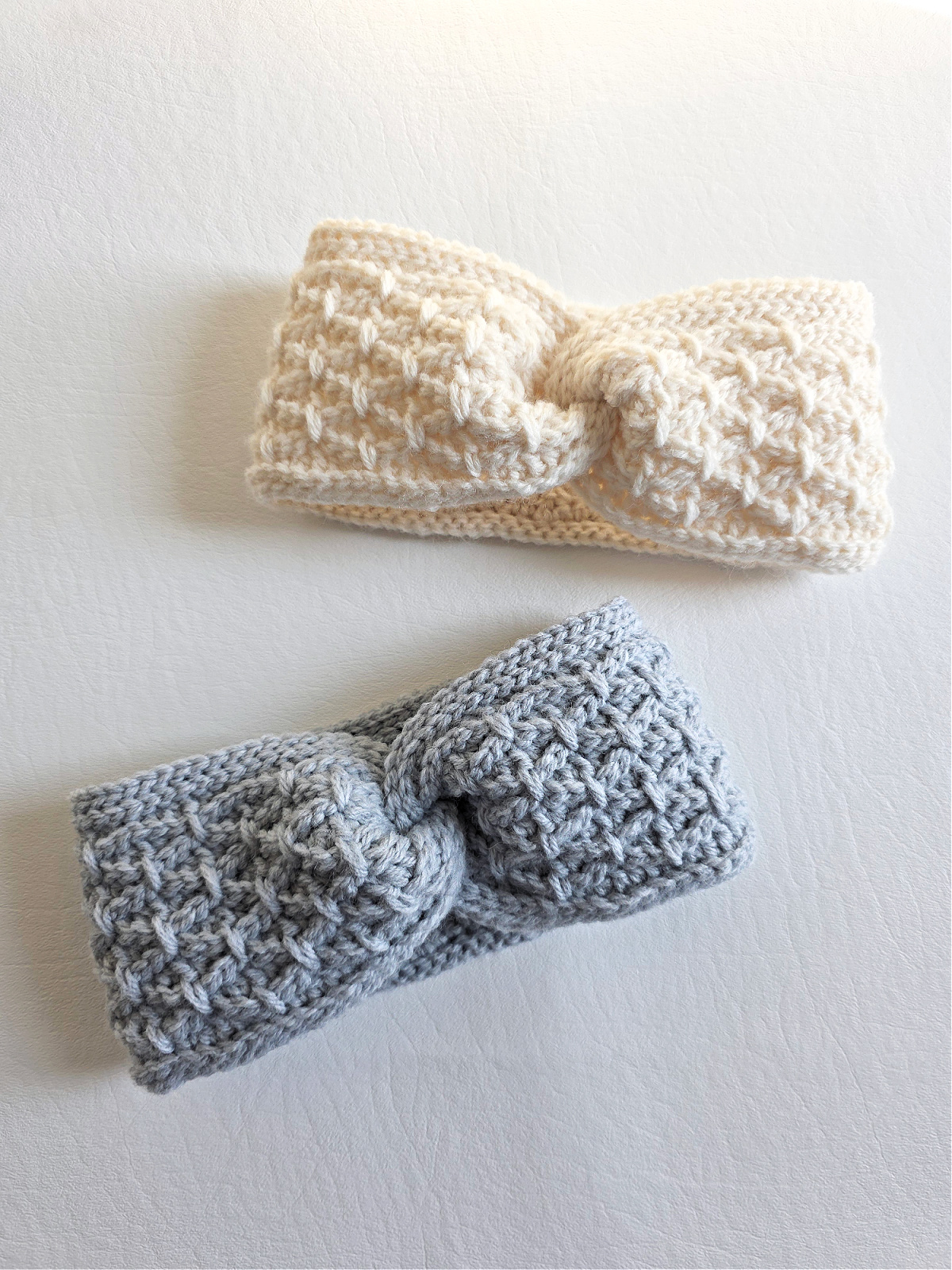 A gray crochet ear warmer and white crochet ear warmer against a white background.