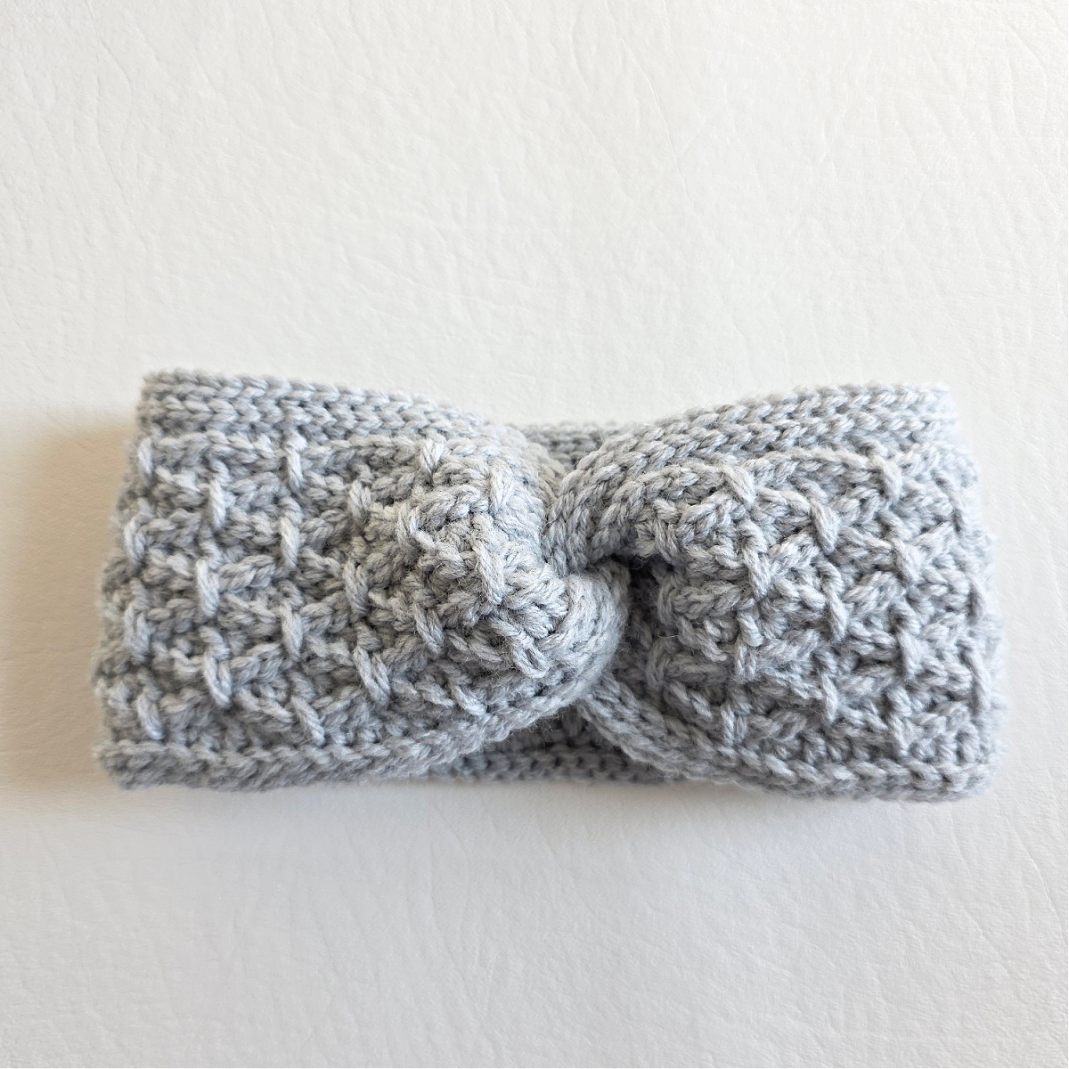 A white twisted crochet ear warmer against a white background.