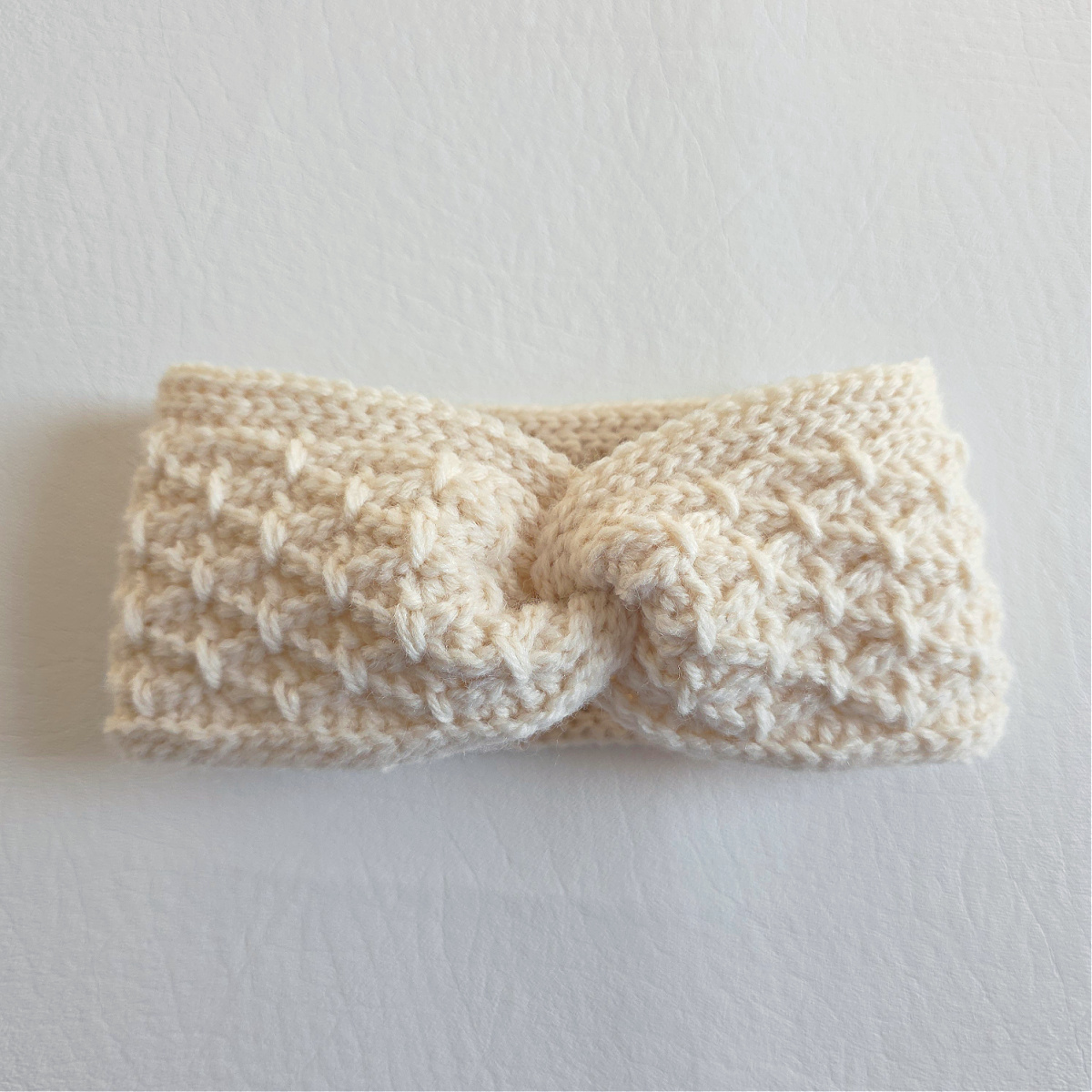 A white twisted crochet head warmer against a white background.