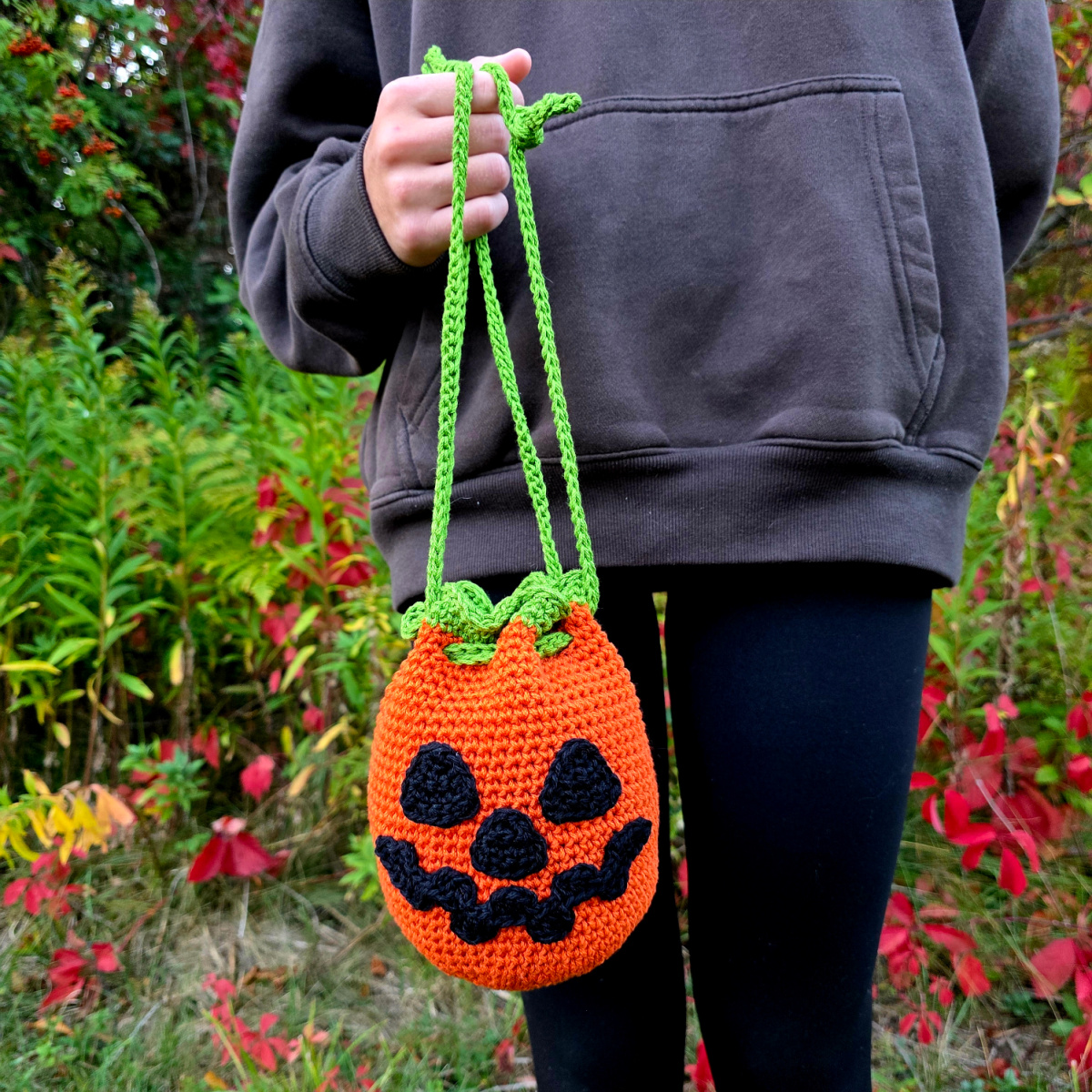 A person standing outside holding a jack-o-lantern drawstring treat bag.