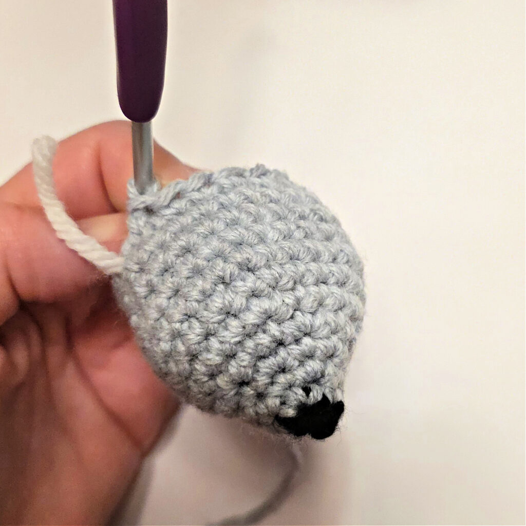A small grey crochet mouse head with a black nose.