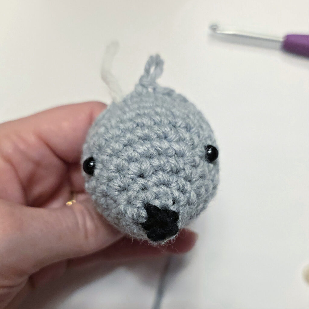 A small grey crochet mouse head with a black nose and safety eyes added.