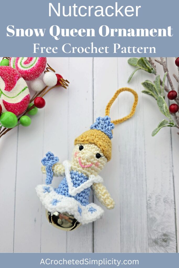 Crochet snow queen ornament laying on a white surface with Christmas candies and greenery.