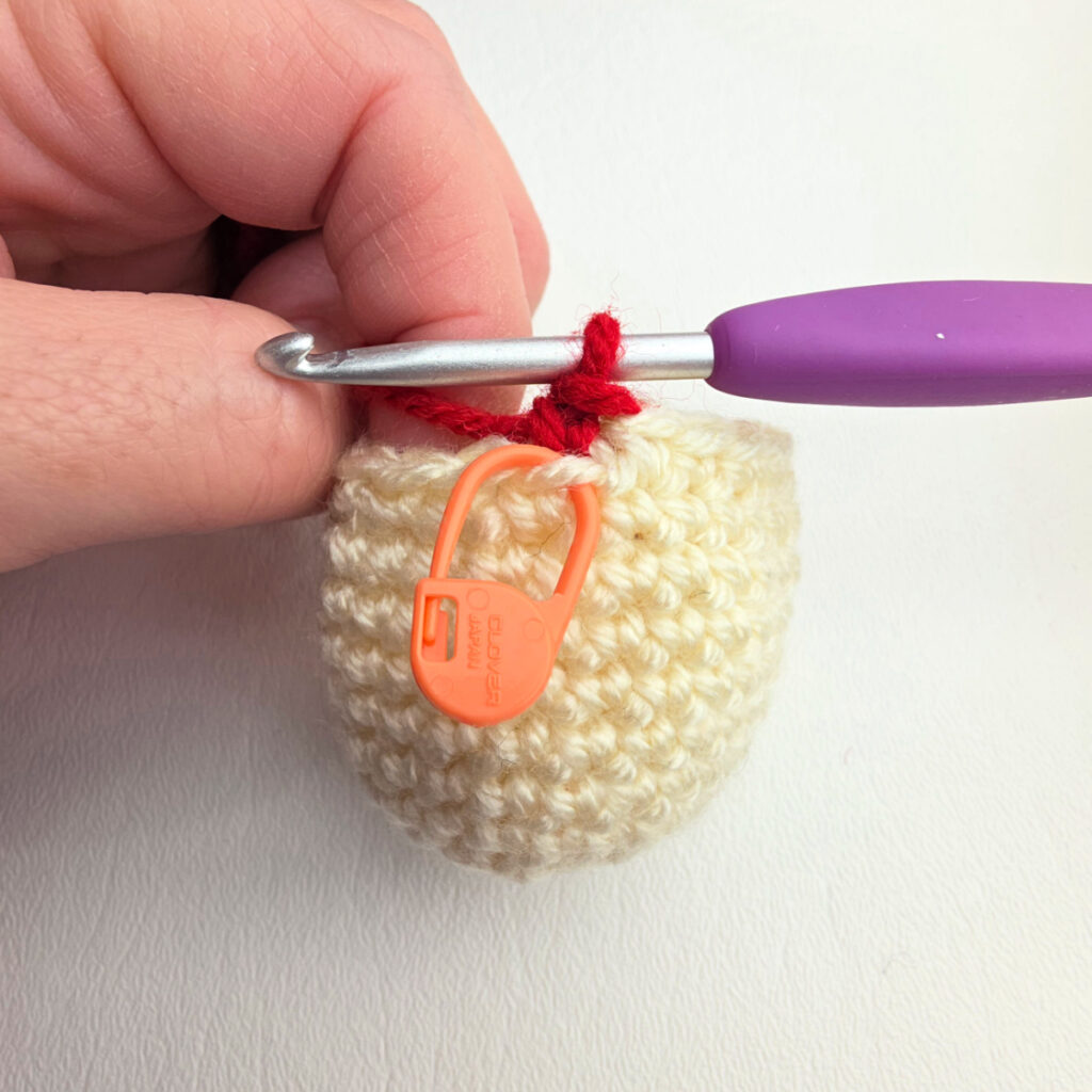 A crochet head for a nutcracker and a purple crochet hook with red yarn to begin crocheting the body.