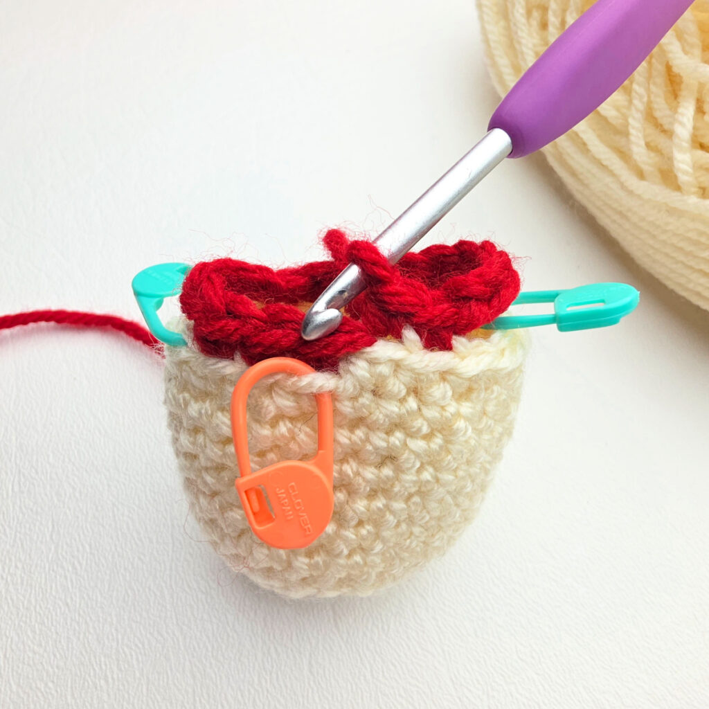 The body of the nutcracker started and armholes created with green and orange stitch markers marking stitches.