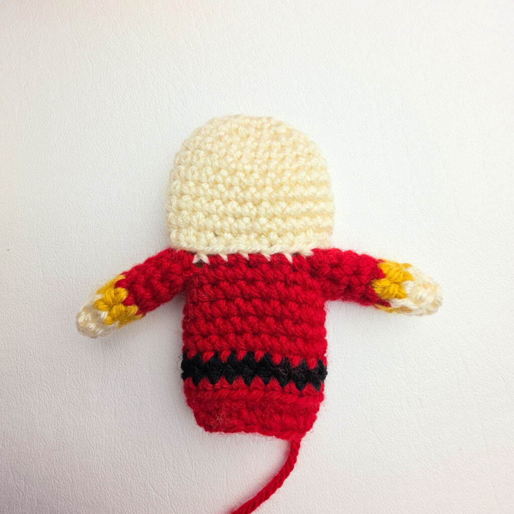 The head, body, and arms of a crochet nutcracker ornament laid flat on a white surface.