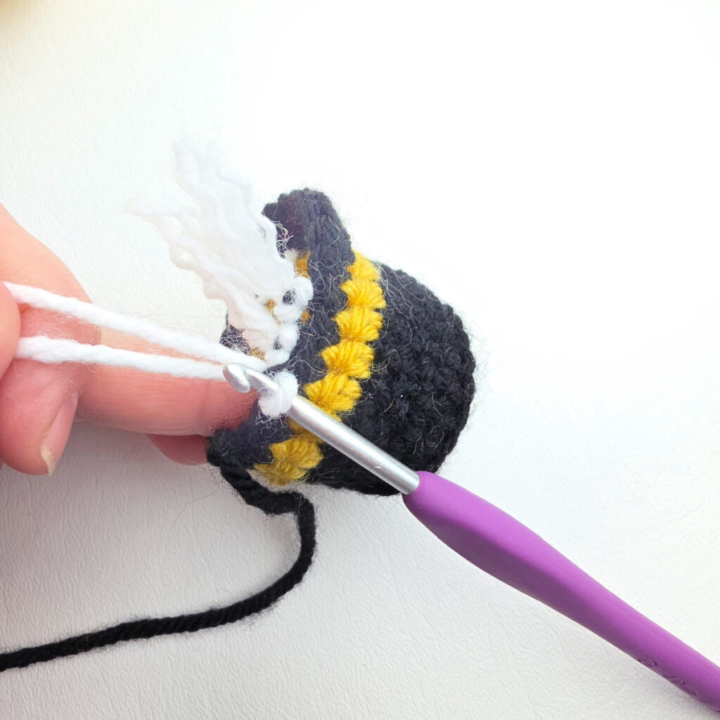 A purple crochet hook adding yarn fringe hair to the edge of the Nutcracker's hat.