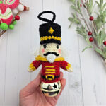 Crochet Nutcracker ornament held in a small hand near Christmas decor.