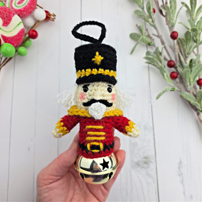 Crochet Nutcracker ornament held in a small hand near Christmas decor.