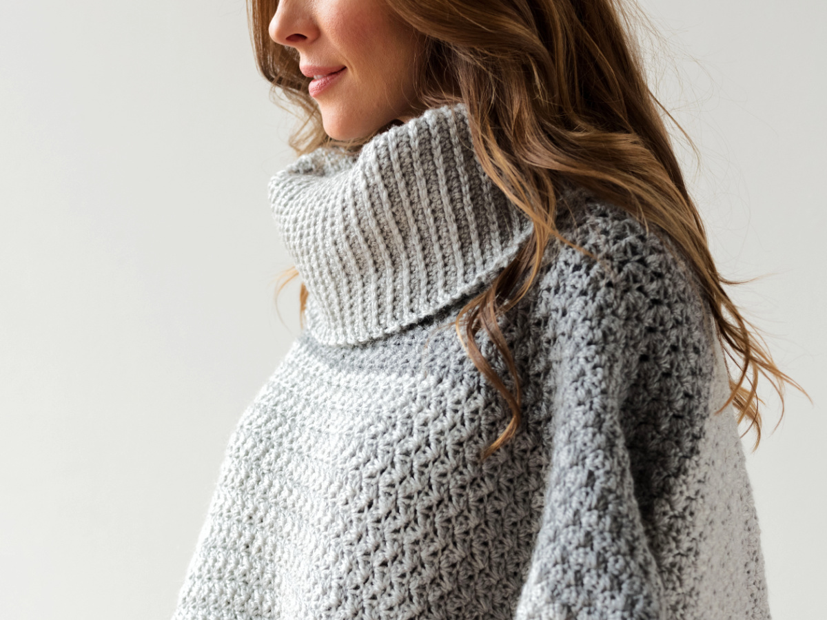 Woman wearing a collared gray poncho with her face turned to the side.