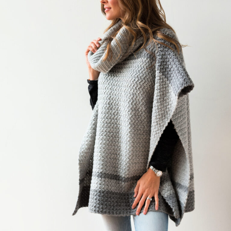 Woman wearing a gray crochet poncho with a wide cowl, blue jeans, and a black undershirt.