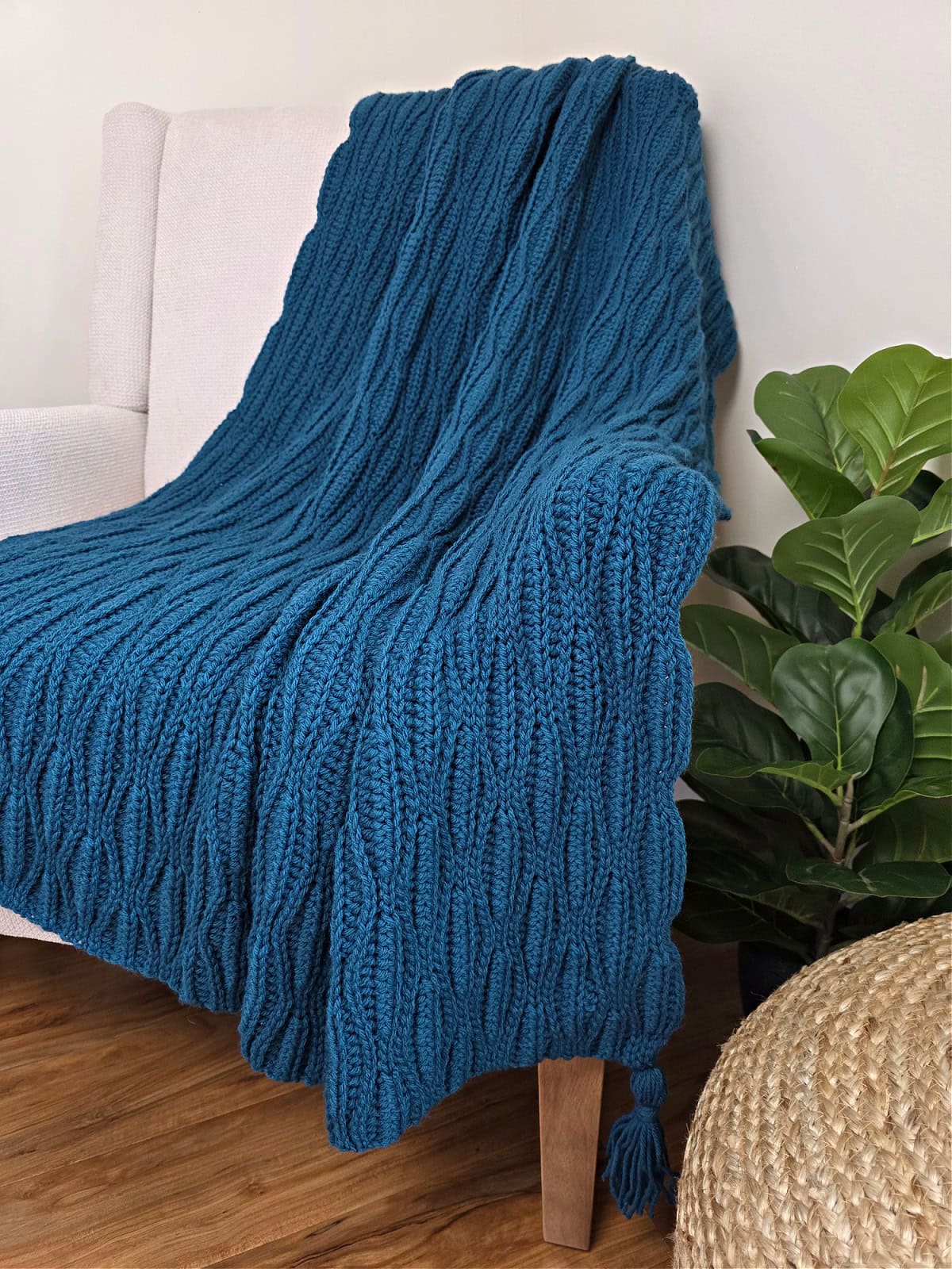 A dark blue crochet blanket draped over a sofa chair with a plant next to it.