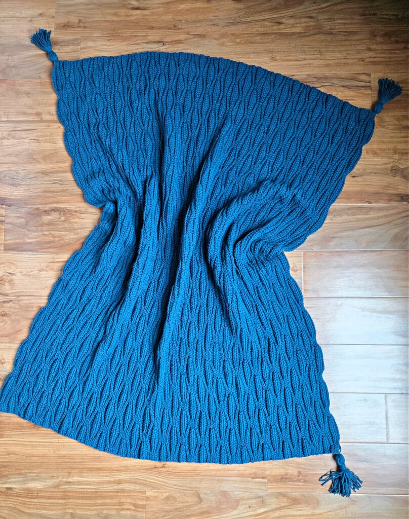 A dark blue crochet blanket spread over a wooden floor.
