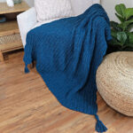 A dark blue crochet blanket draped over a sofa chair and wooden floor with a cushion next to it.