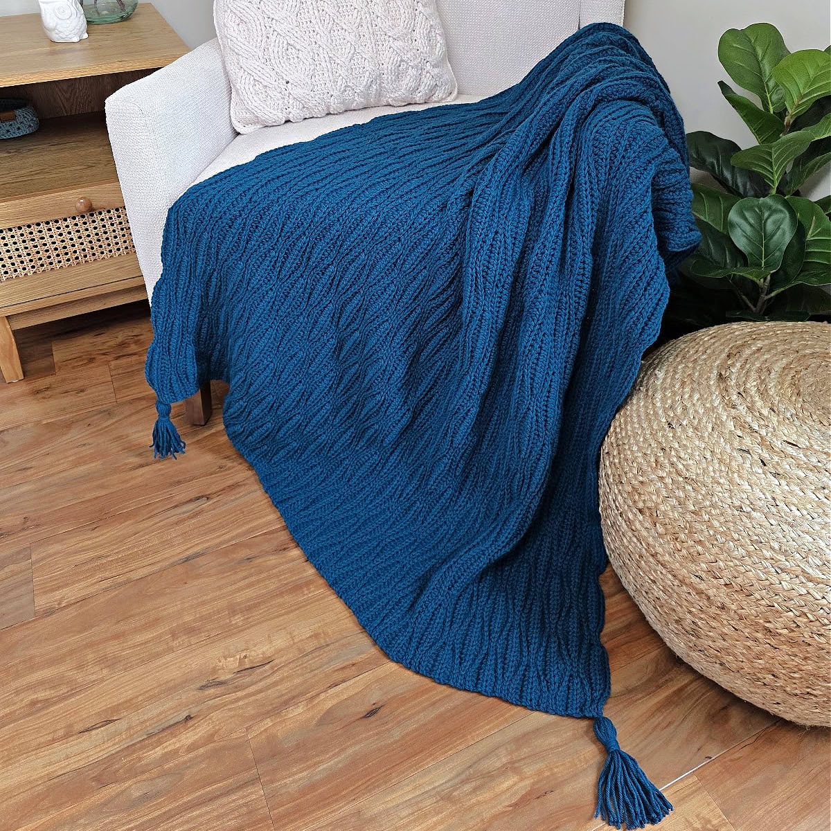 A dark blue crochet blanket draped over a sofa chair and wooden floor with a cushion next to it.