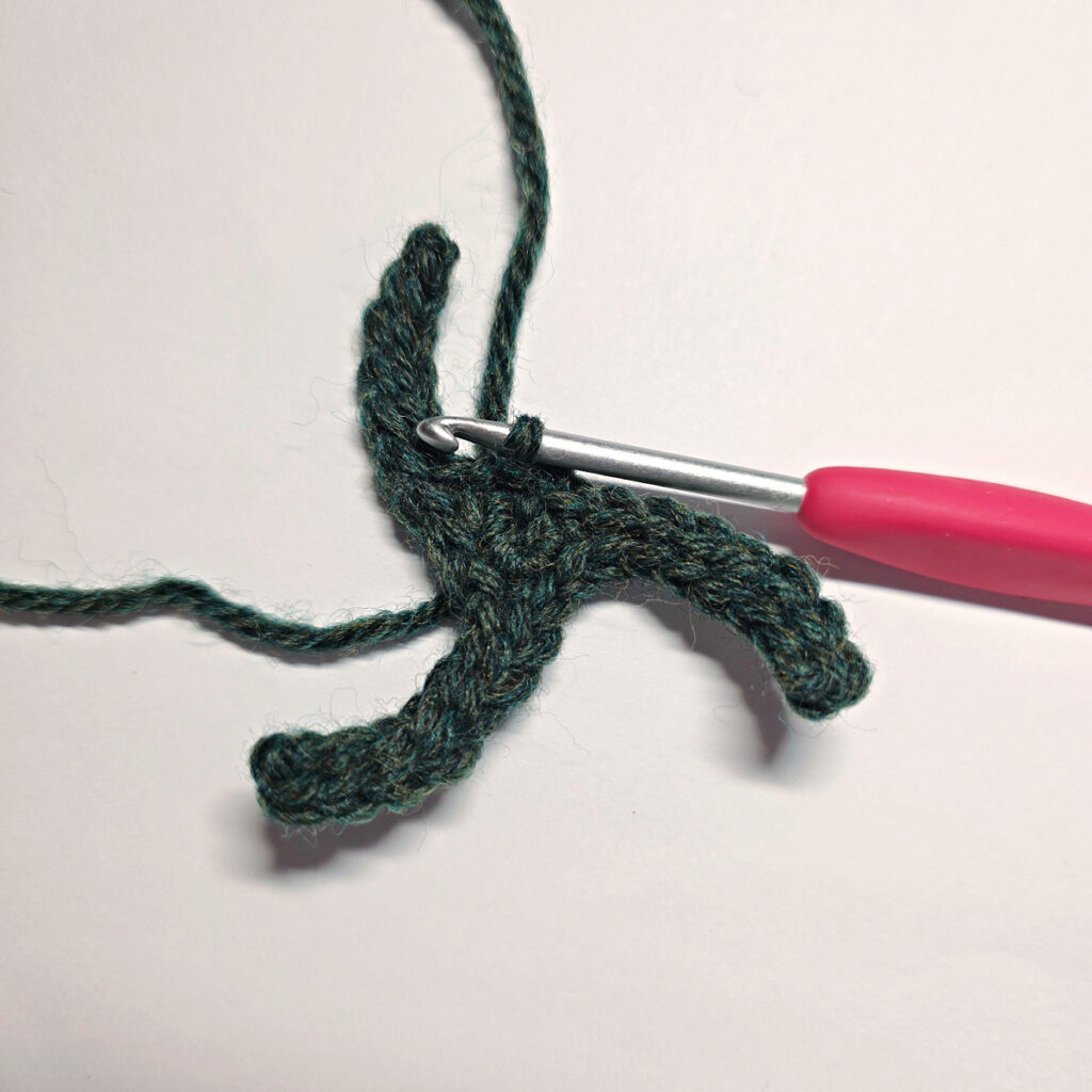 Rounds one and two of green crochet poinsettia leaves with a red crochet hook.