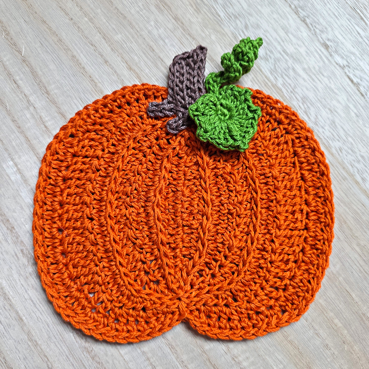 Large orange crochet pumpkin with a brown stem and green leaves against a wooden background.