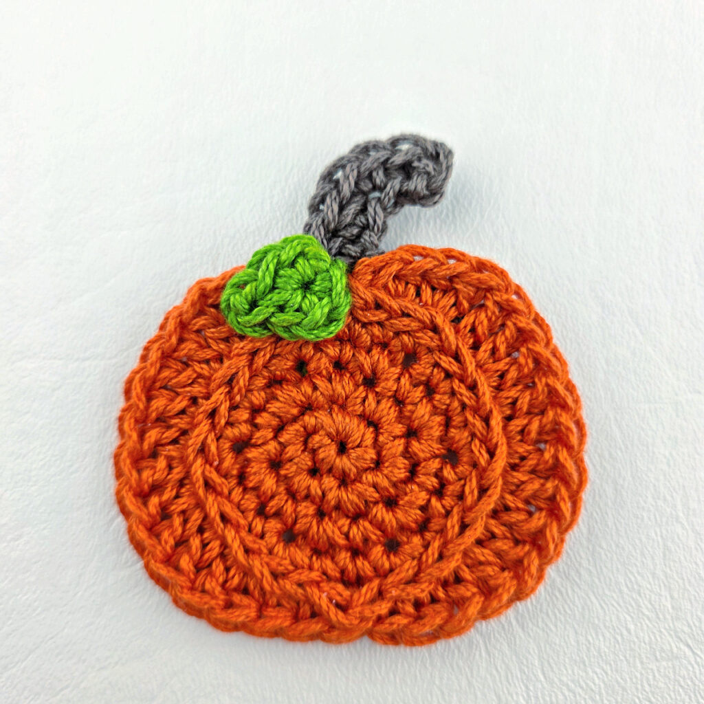 Attaching a crochet pumpkin leaf to the pumpkin applique.