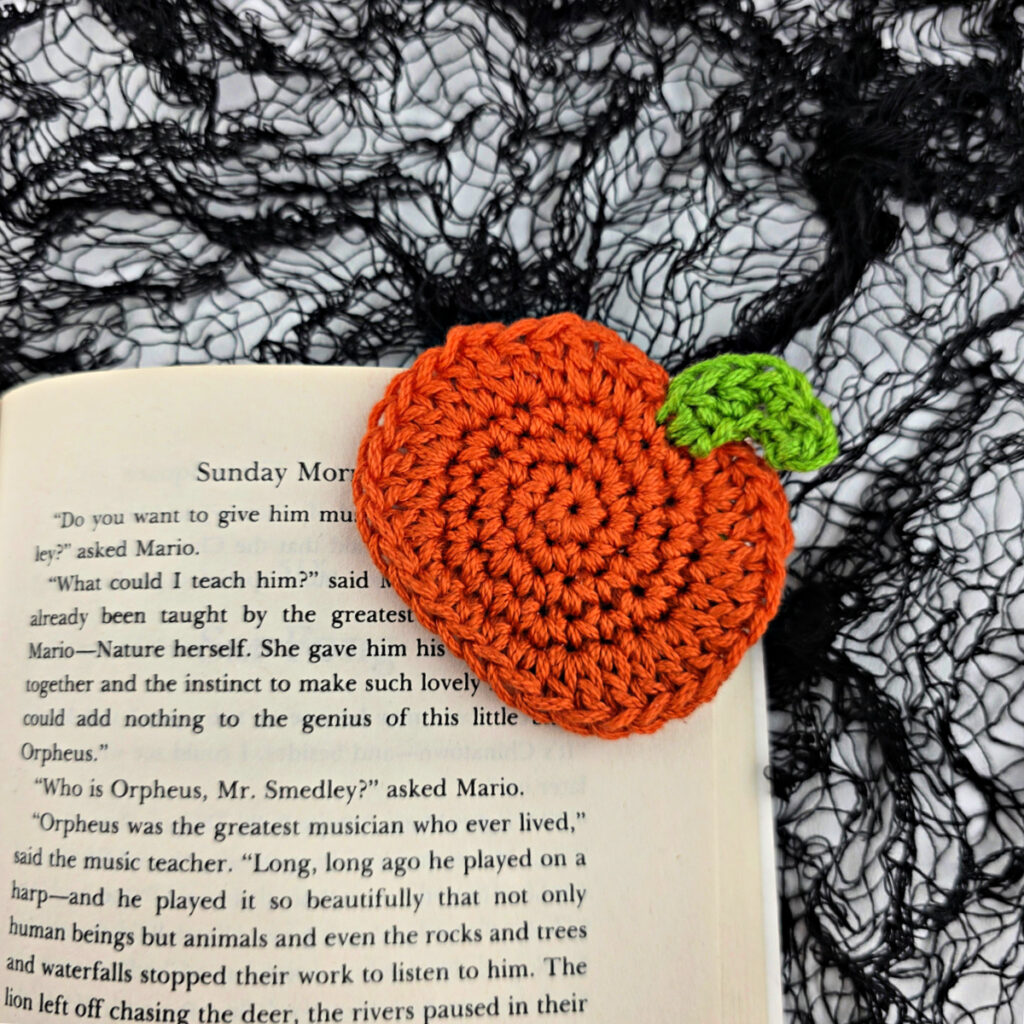 A crochet pumpkin bookmark attached to a book.