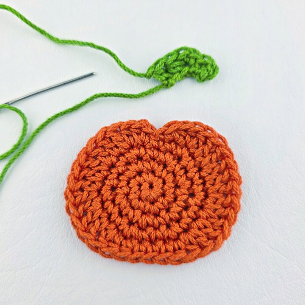 An orange crochet pumpkin with a green stem.