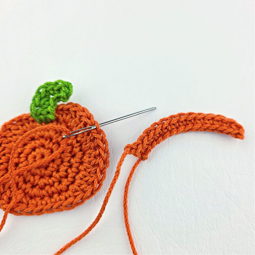 An orange crochet pumpkin with a green stem.