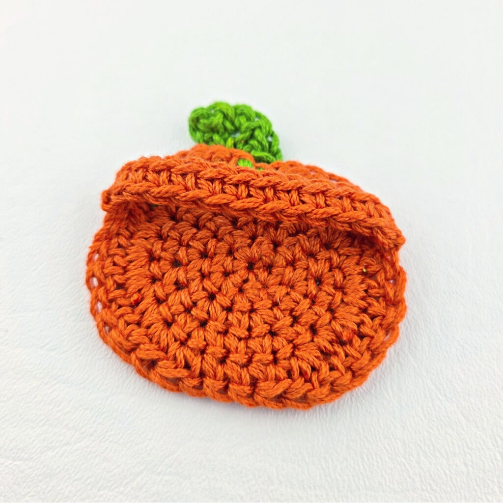 A crochet pumpkin with a green stem.