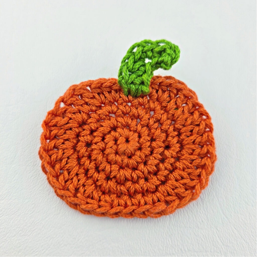 A crochet pumpkin with a green stem.