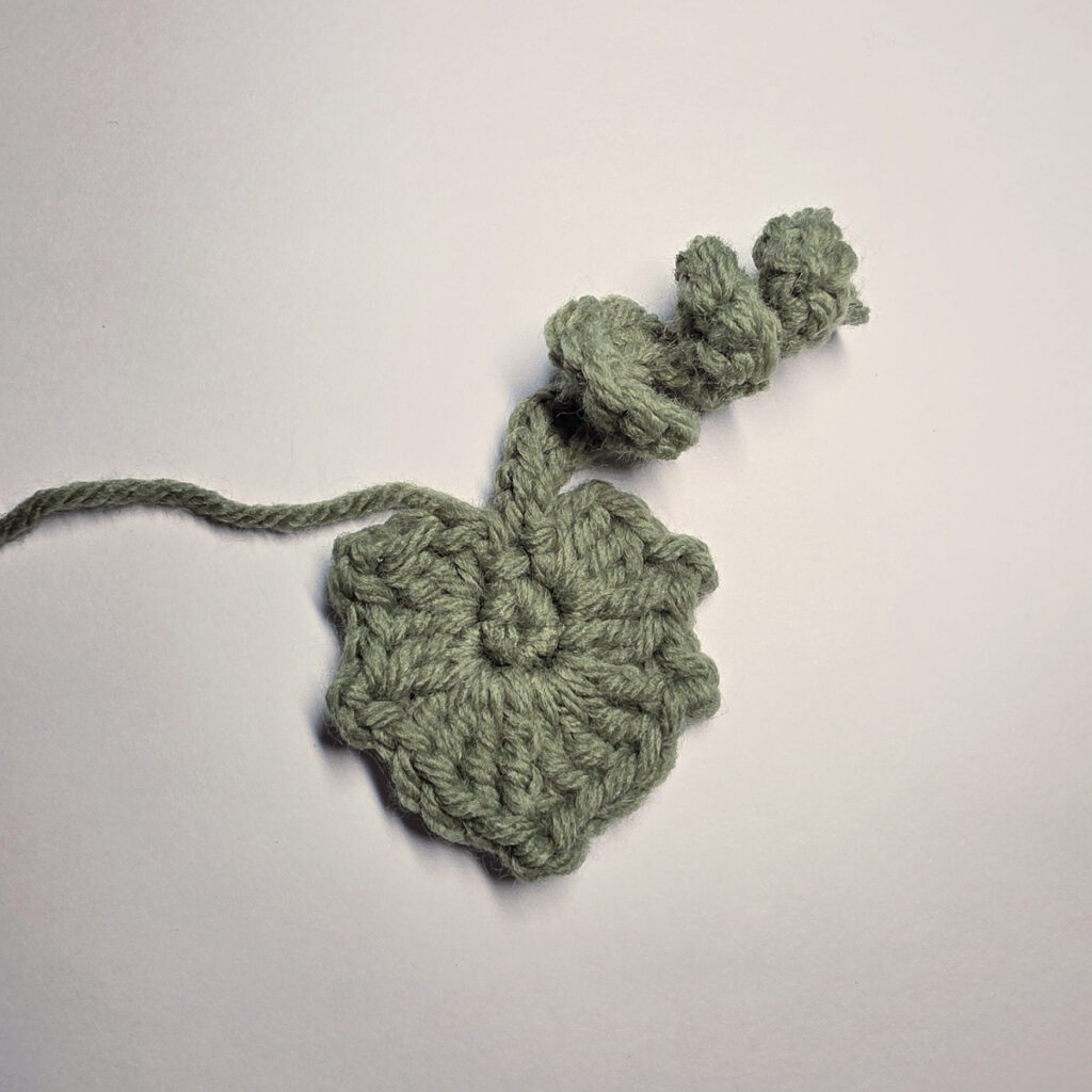 A green crochet leaf against a plain background.